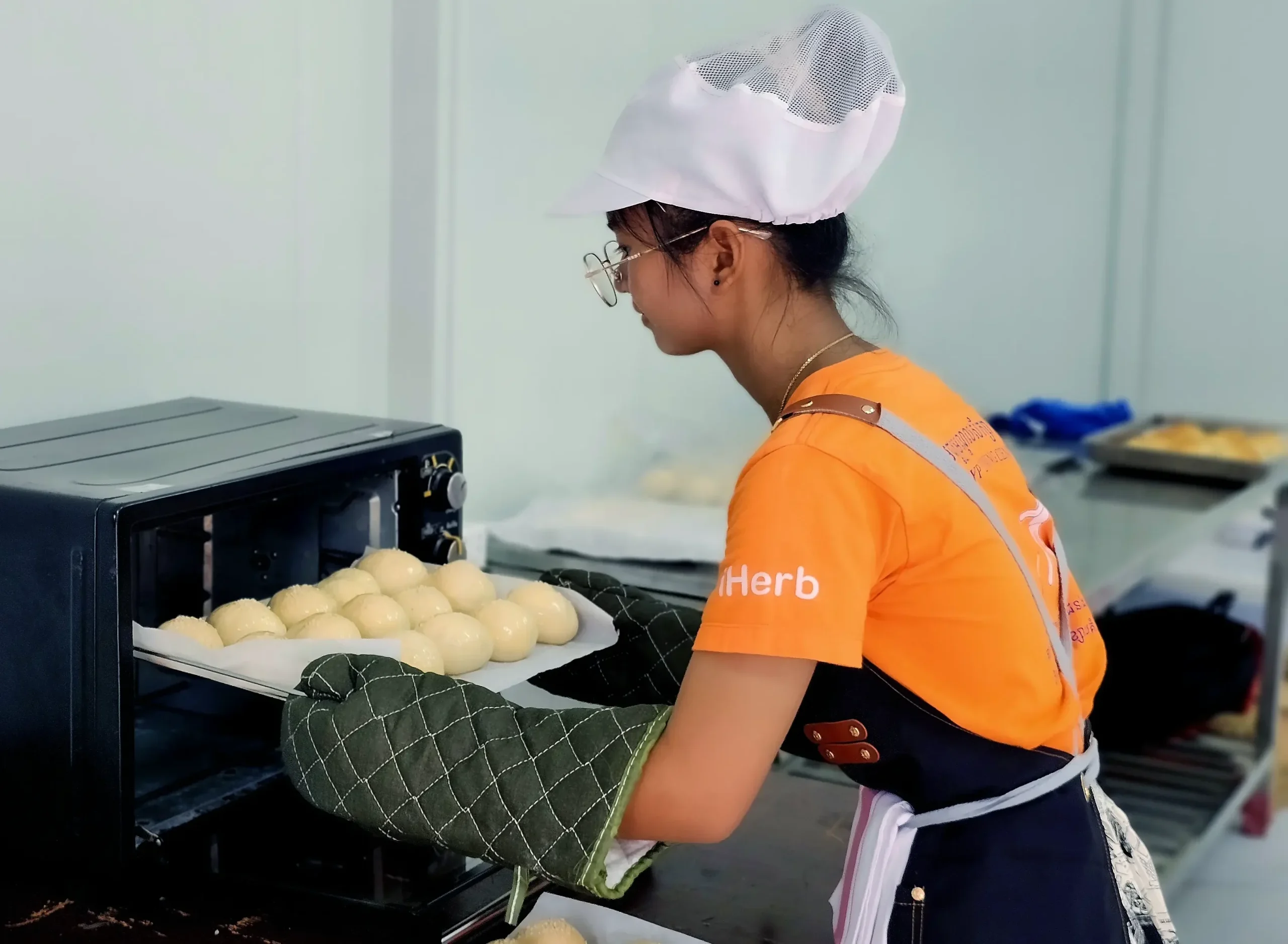 Learner baking fresh bread rolls during vocational training at the DYP Inclusive Café and Bakery in Cambodia