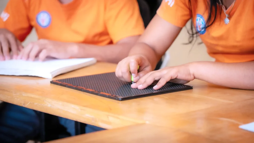 Close-up of a student writing Braille using a slate and stylus at the DYP Learning Center in Cambodia.