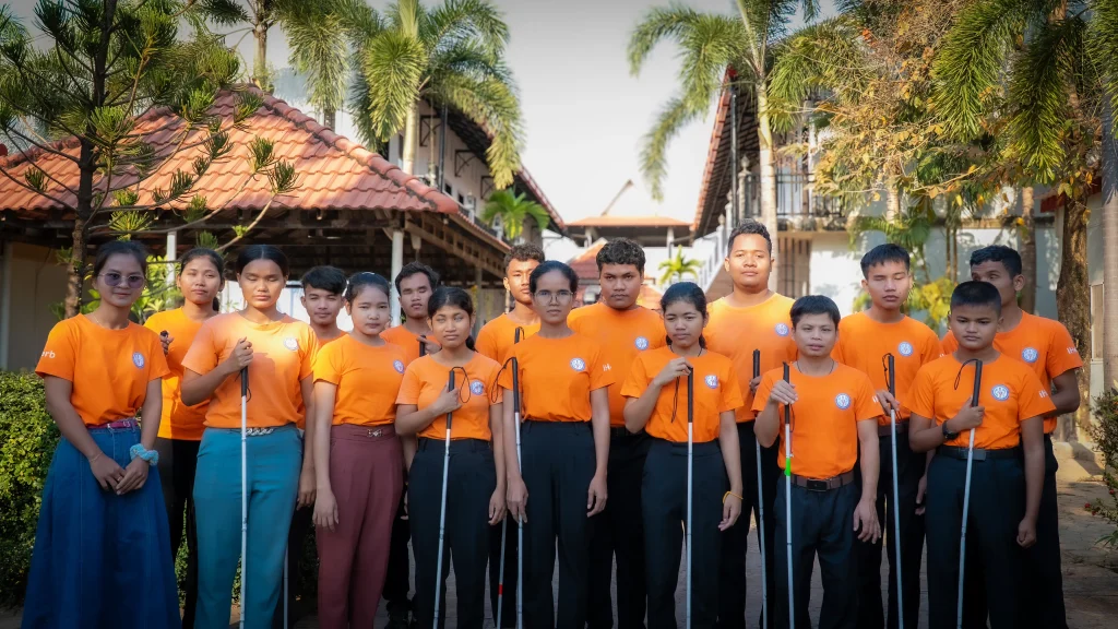 Students with visual impairments standing together at the DYP Learning Center in Cambodia, holding white canes and wearing DYP uniforms.