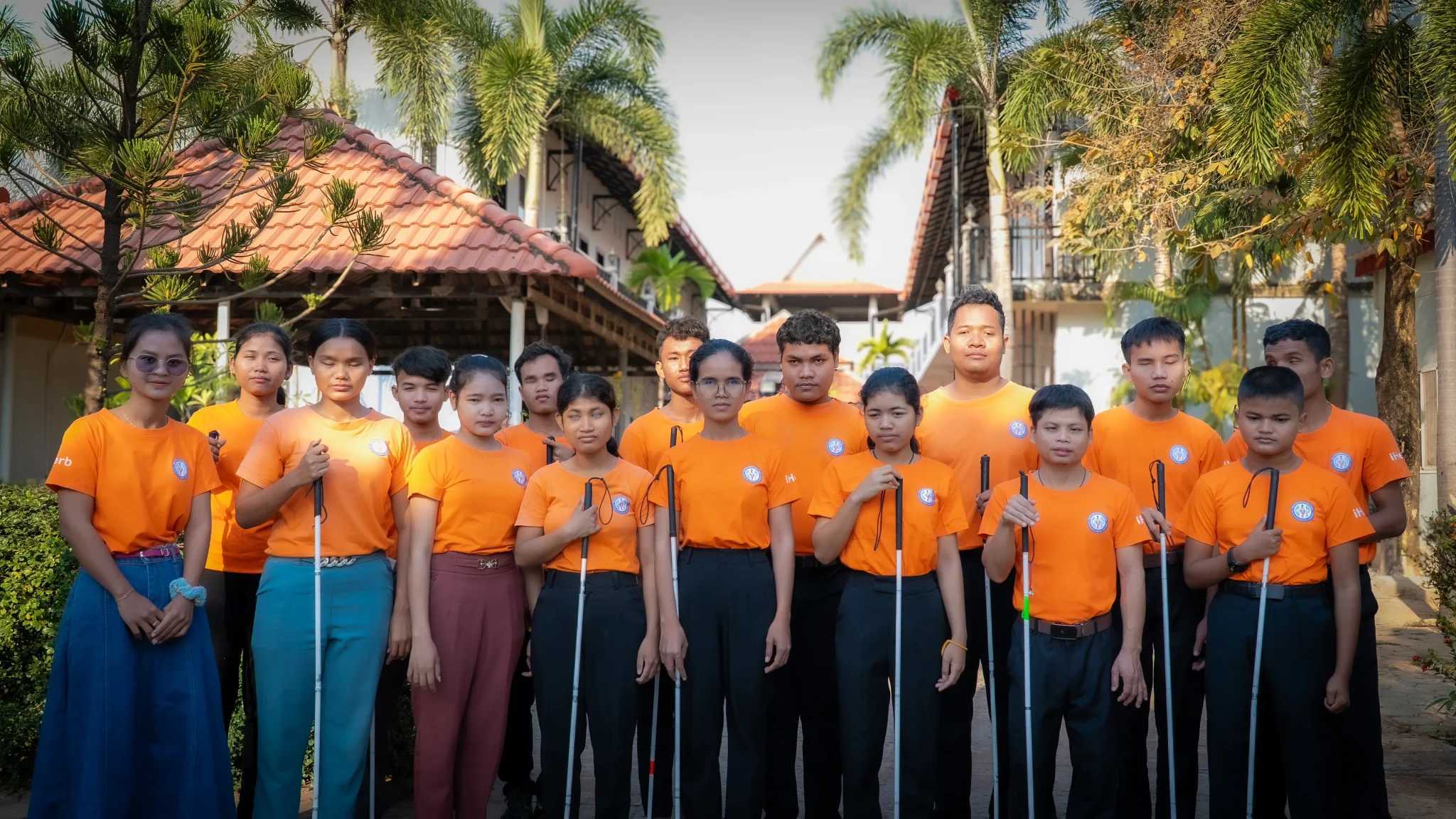 Students with visual impairments standing together at the DYP Learning Center in Cambodia, holding white canes and wearing DYP uniforms.
