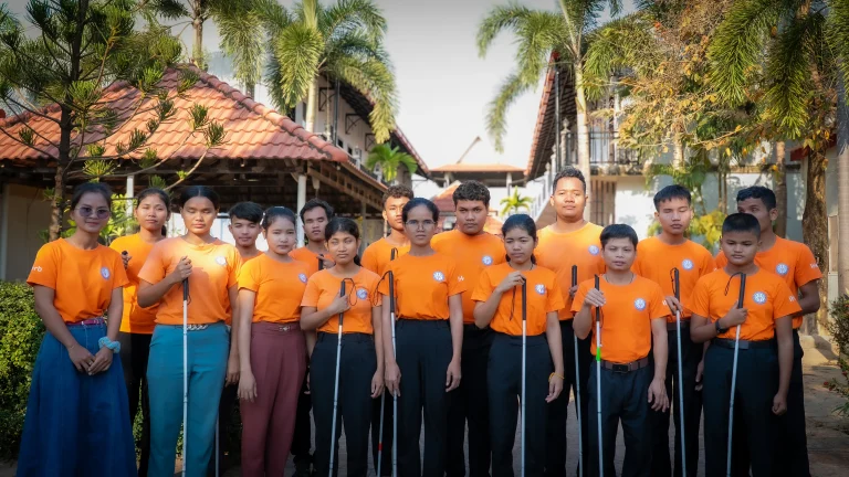 Students with visual impairments standing together at the DYP Learning Center in Cambodia, holding white canes and wearing DYP uniforms.