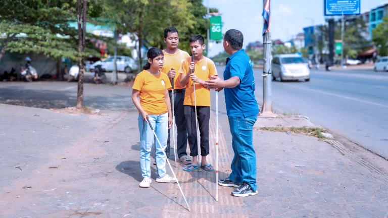 Students with visual impairments practicing white cane mobility training on a street in Cambodia.