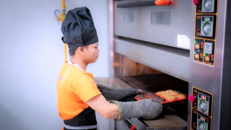 Learner with visual impairment baking pastries in an oven during training at the DYP Inclusive Café & Bakery in Siem Reap.