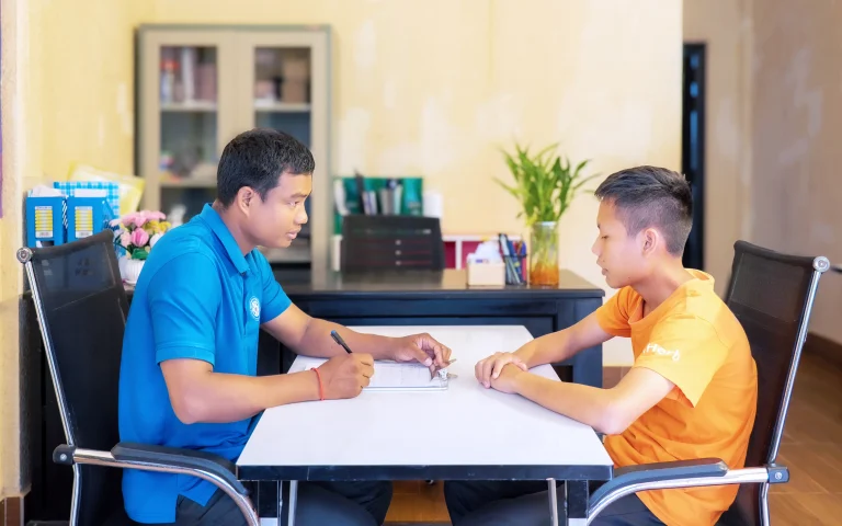 Counselor meeting with a visually impaired student to discuss progress and support at the DYP Learning Center in Cambodia.