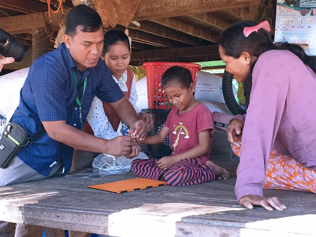 DYP staff supporting a child with visual impairment learning braille in a rural community in Cambodia