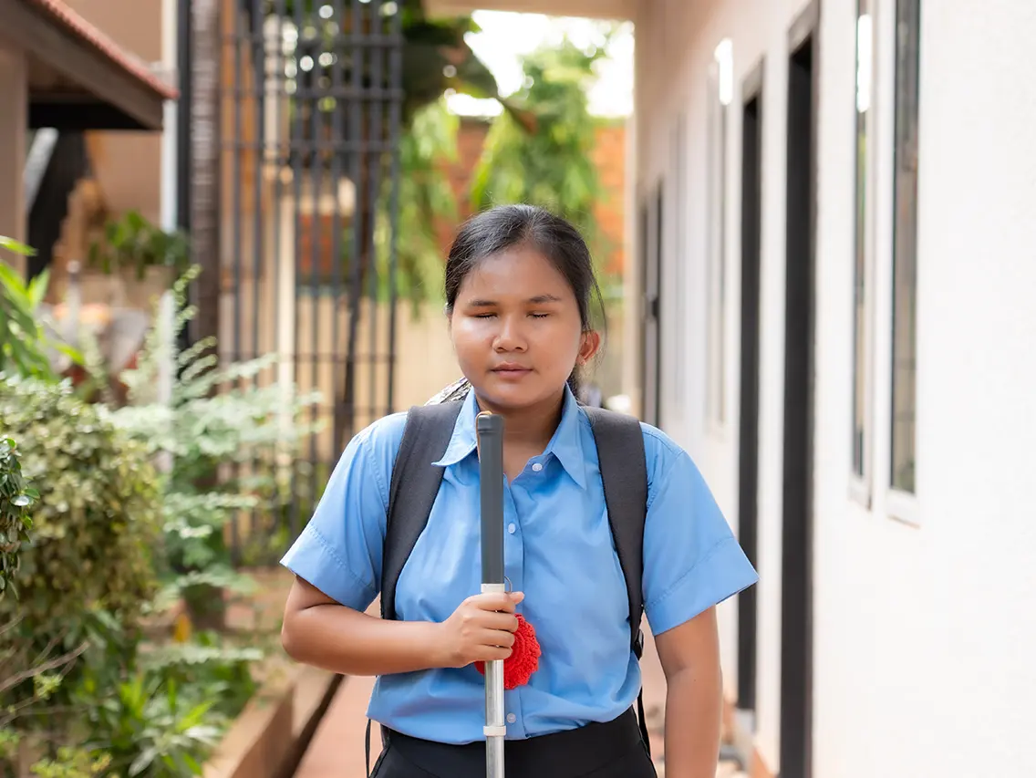 Sreyvat using a white cane while carrying her school backpack at DYP Cambodia